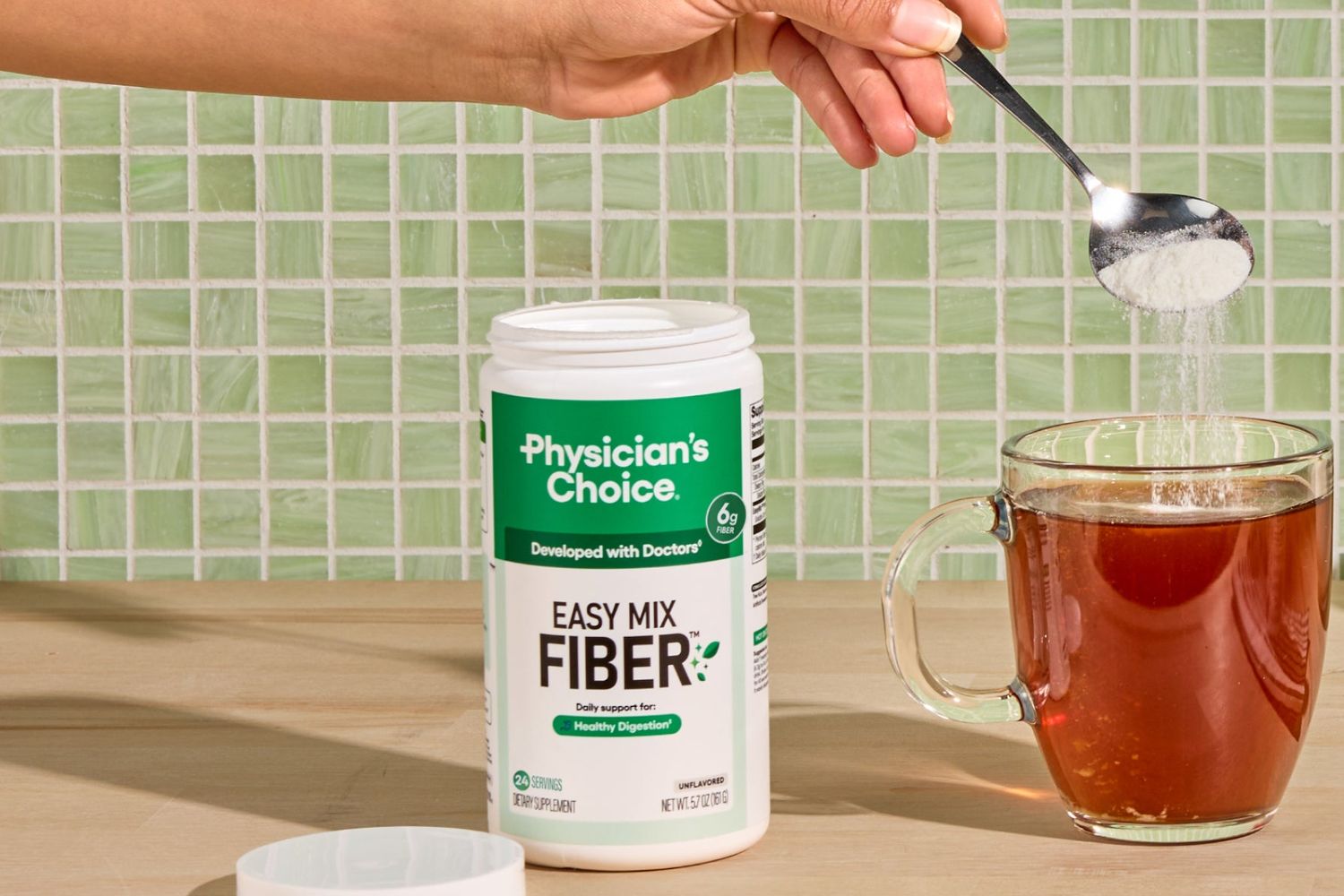 A heaping spoonful of Easy Mix Fiber being stirred into a mug of tea beside the open tub